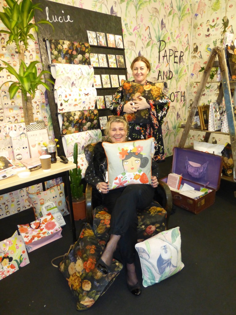 Lucie Chadderton (standing) on the Sooshichacha stand at Top Drawer with London agent Beth Robson modeling some of the new furnishings products.